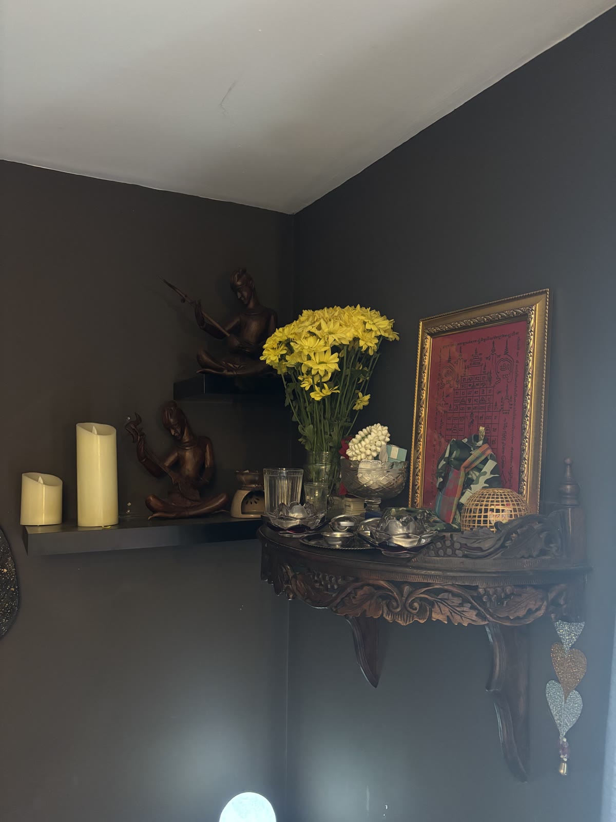 Fresh yellow flowers beside small wooden Thai figures and a framed sacred cloth