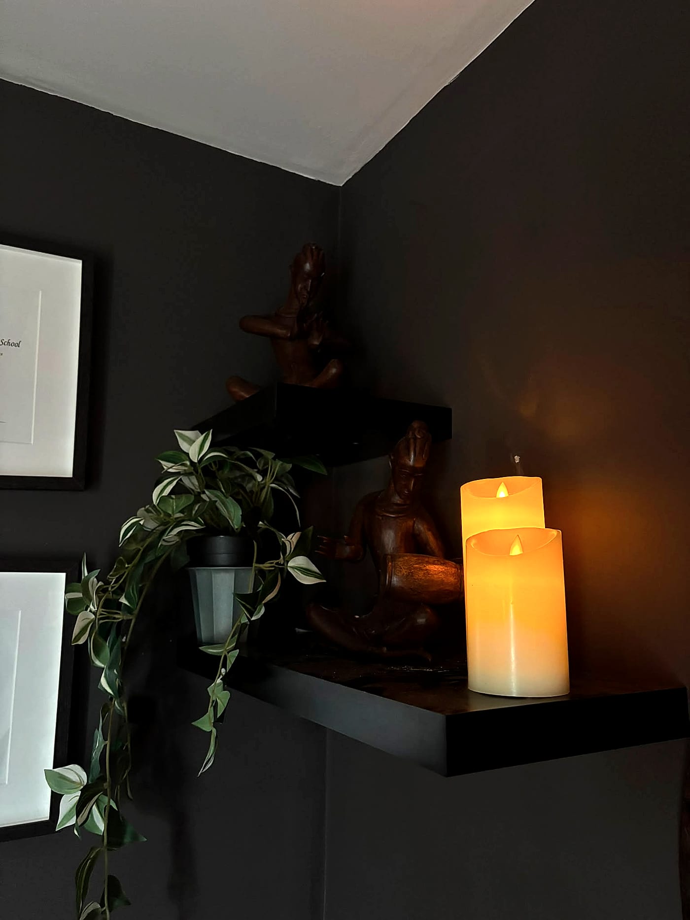 Two hand-carved wooden musician statues on a corner shelf, lit by warm candlelight beside a trailing plant