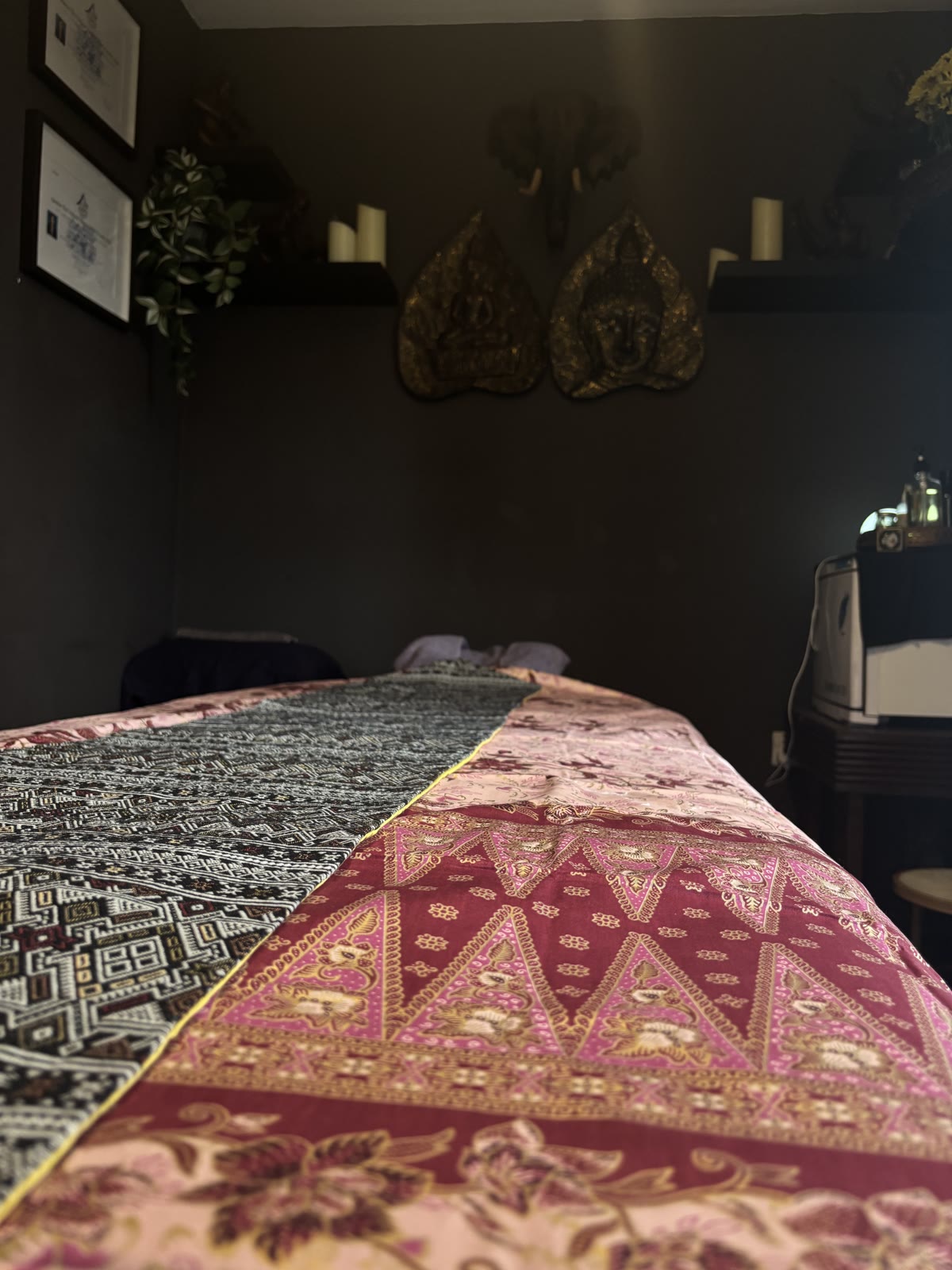Carved wooden Buddha masks and an elephant head ornament on the wall above the treatment bed