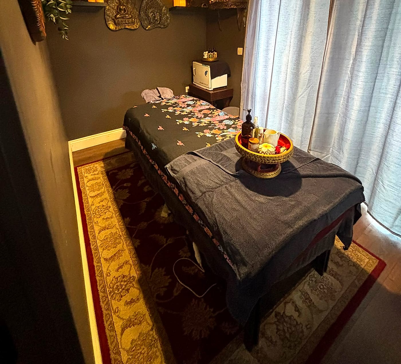 The foot of the treatment table styled with a golden tray of oils and a lotus flower, beside sheer curtains